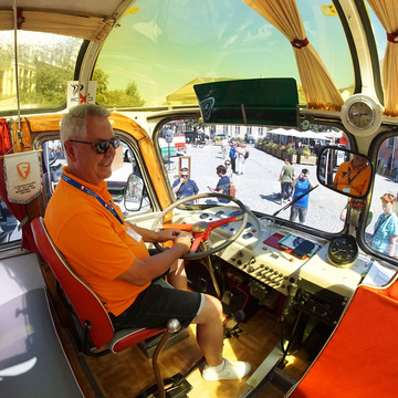 Ein Mann sitzt am Steuer eines alten Busses. Der Innenraum sieht gepflegt aus.
