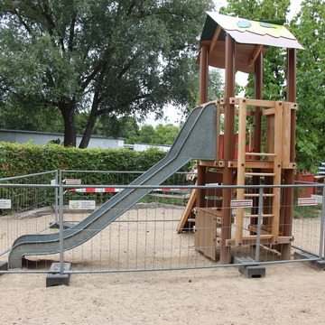 Ein Spielturm mit einer Rutsche. Um das Gerät steht noch ein Bauzaun.