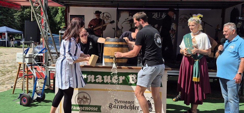 Vier Personen stehen um ein Bierfass herum. Eine von ihnen sticht das Bierfass an. 