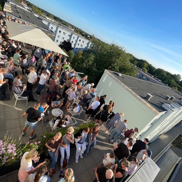 Mehrere Menschen auf der Dachterrasse mit Blick in Richtung Sonne.