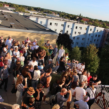 Mehrere Menschen auf der Dachterrasse mit Blick in Richtung Sonne. 
