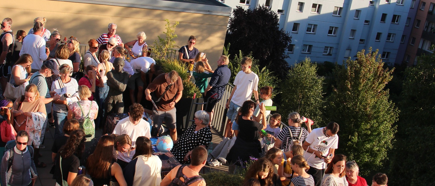 Mehrere Menschen auf der Dachterrasse mit Blick in Richtung Sonne. 