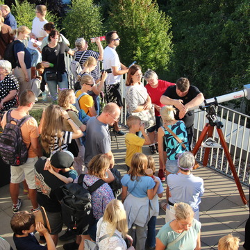 Mehrere Menschen auf der Dachterrasse mit Blick in Richtung Sonne. 