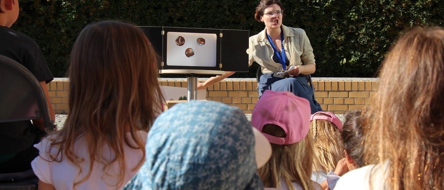 Eine Frau sitzt neben einerm Kamishibai, einem japanischen Erzähltheater und liest Kindern vor. 