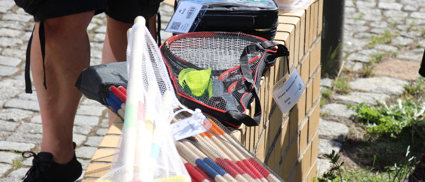 Auf einer Steinmauer liegen verschiedene Outdoorspiele, wie Badminton, Krocket un Wikinger Schach. 