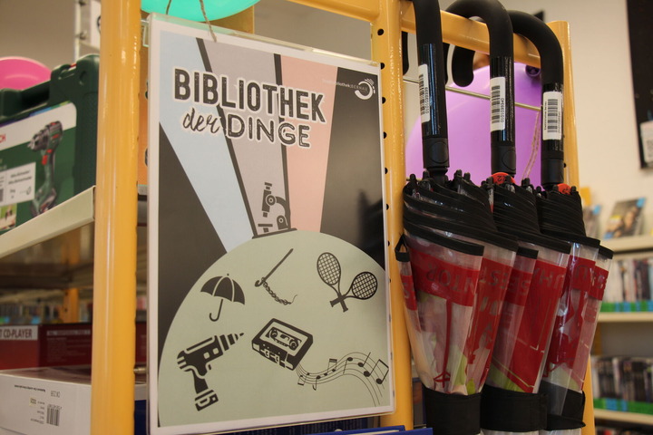 Ein Regal in der Bibliothek ist mit "Bibliothek der Dinge" überschrieben. Im Regal liegt ein Akkuschrauber, ein CD-Player und Regenschirme zum ausleihen. 