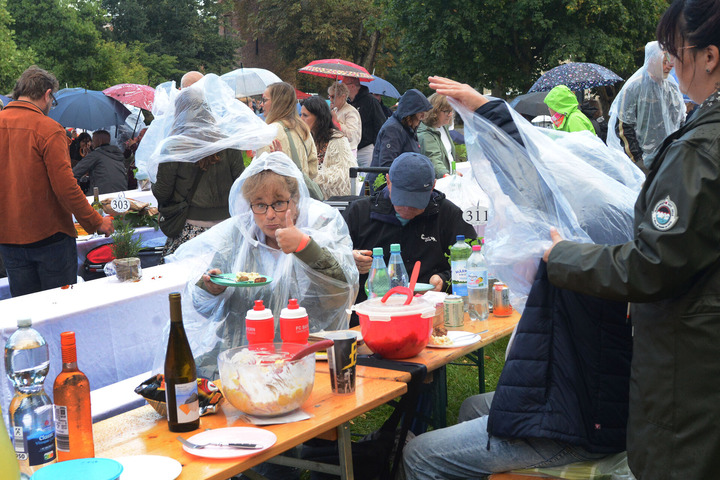 An Bierbänken sitzen mehrere Menschen in Regenponchos und speisen. Eine Frau hält den Daumen nach oben. 
