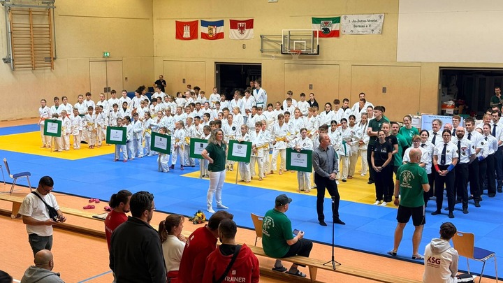 In einer Sporthalle stehen mehrere Kämpferinnen und Kämpfer in Formation 