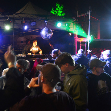Das Bild zeigt eine Bühne mit DJ und Publikum von der vorherigen Lokaltour