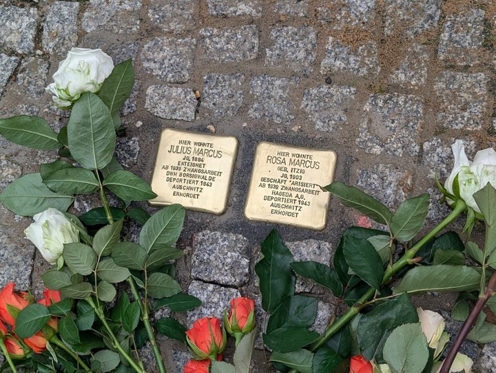 Auf dem Bild sieht man zwei goldfarbene Stolpersteine im Gedenken an das Ehepaar Rosa und Julius Marcus. Rosen wurden dort abgelegt.