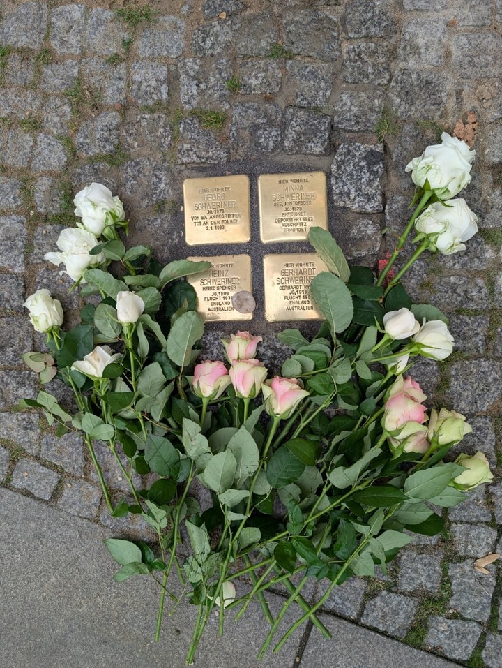 Auf dem Bild sieht man vier goldfarbene Stolpersteine im Gedenken an die Familienmitglieder Schweriner. Rosen wurden dort abgelegt.