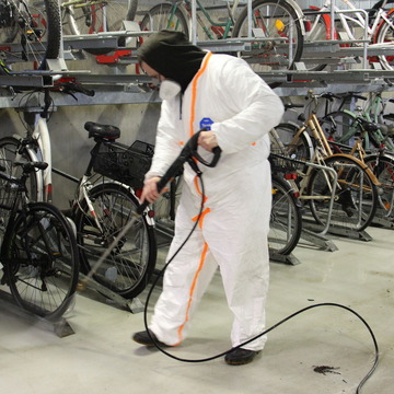Eine Reinigungsfachkraft in weißem Anzug reinigt mit einem Hochsdruckstrahler das Fahrradparkhaus. 