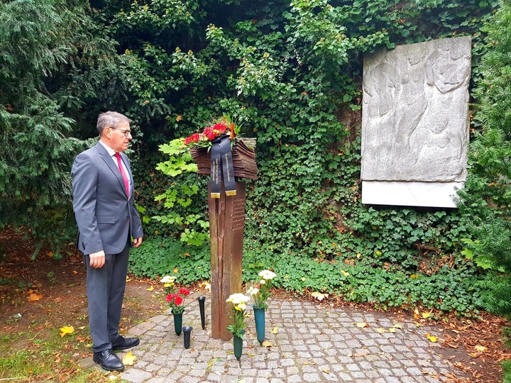 Bürgermeister André Stahl hält vor dem Konrad-Wolf-Denkmal im Stadtpark inne. An Denkmal sind Blumen angelegt.
