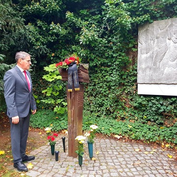 Bürgermeister André Stahl hält vor dem Konrad-Wolf-Denkmal im Stadtpark inne. An Denkmal sind Blumen angelegt.