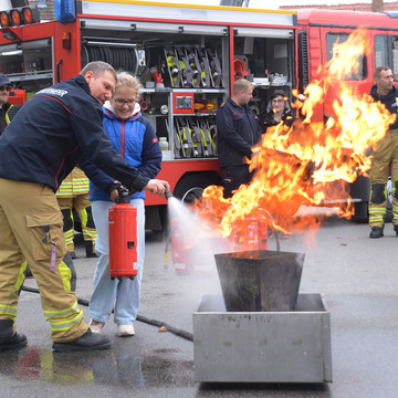 Feuerlöschübung mit einer jungen Frauen und unter Anweisung der Feuerwehrleute.
