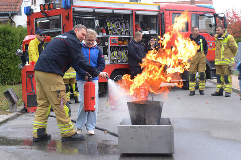 Feuerlöschübung mit einer jungen Frauen und unter Anweisung der Feuerwehrleute.