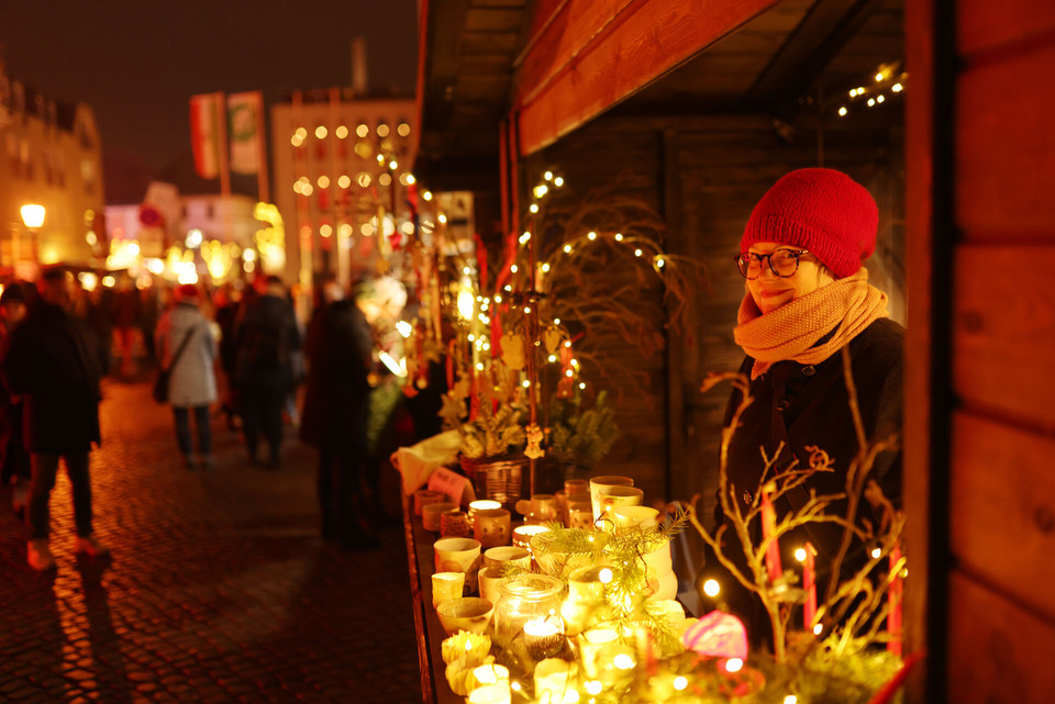 Auf einem Weihnachtsmarkt steht ein Stand an dem Gläser und Gefäße für erzen angeboten werden. Die Händlerin am Stand lächelt in die Kamera
