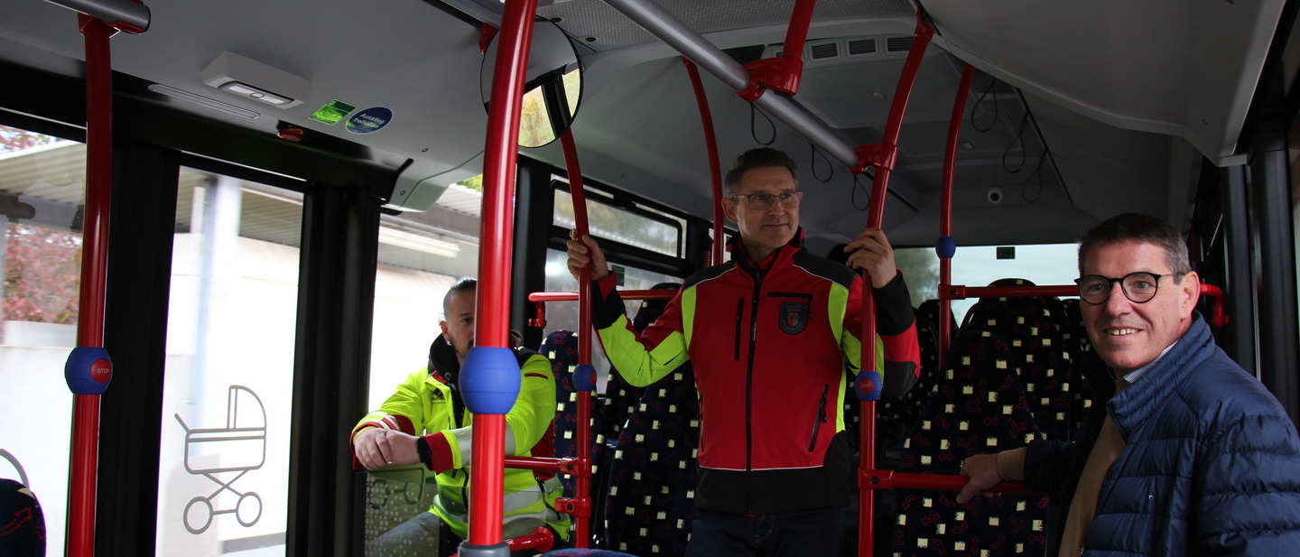 Drei Männer stehen im Rettungsbus, der von innen wie in Liniebus aussieht. 